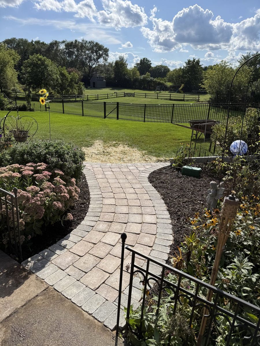 New curved paver walkway between mulch beds and black fencing, after