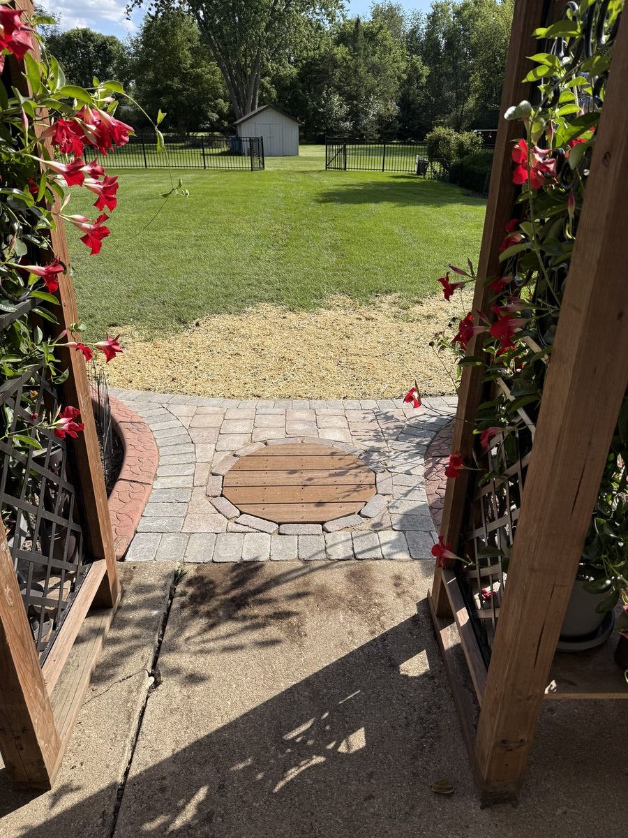 New paver walkway with a round wood inlay at the arbor entrance, after