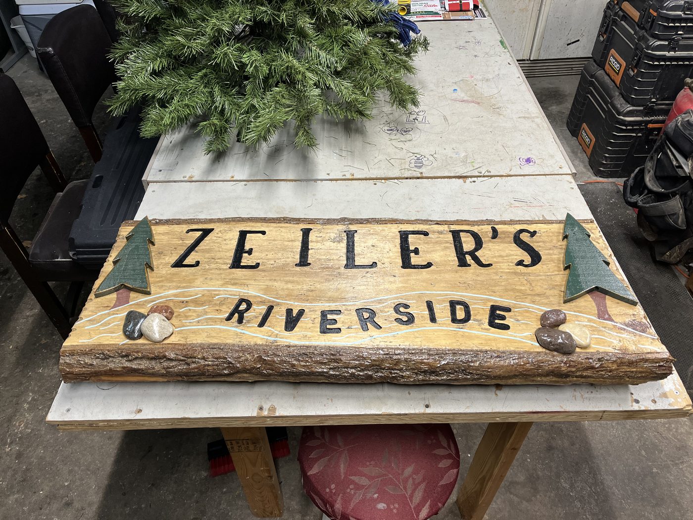 Custom carved wood sign reading Zeiler's Riverside with pine tree accents